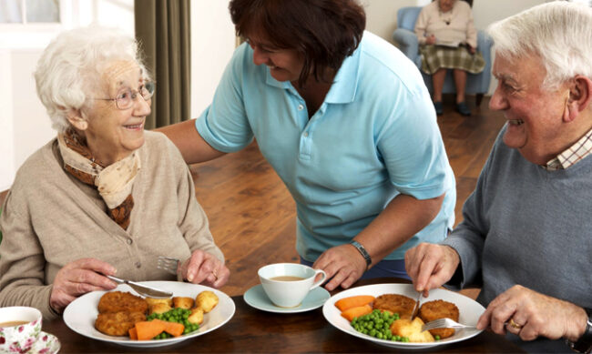 Cuidadora sirviendo un menú saludable a personas de la tercera edad
